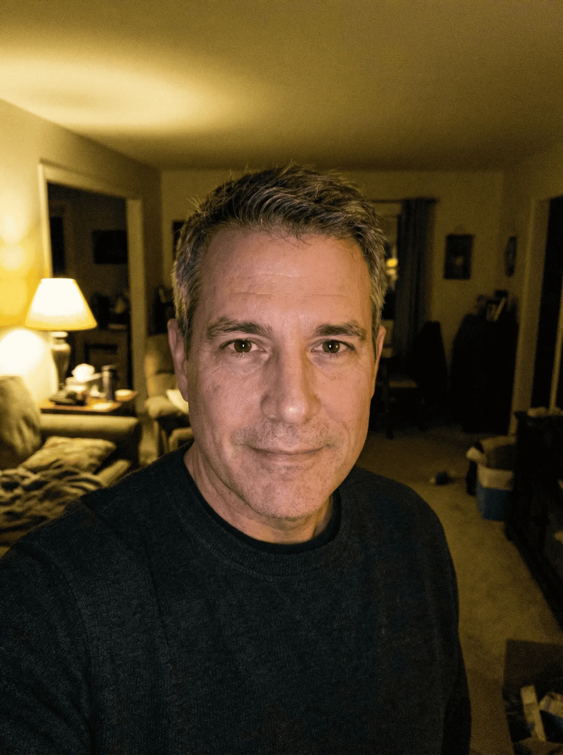 Home selfie of a man in a dark sweater in a dim living room
